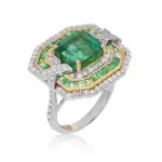 Art deco emerald ring featuring Zambian emerald with tripple halo of round cut diamonds and baguette cut emeralds; crafted in white gold with yellow gold basket