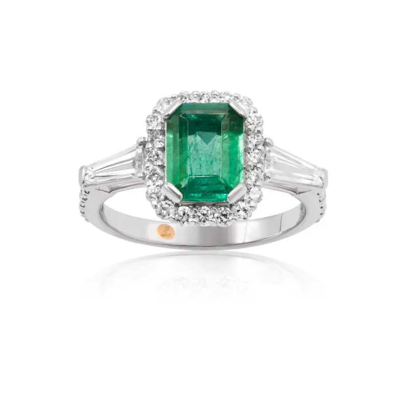 Emerald engagement ring with diamonds in the shape of tapered baguettes as side stones and a diamond halo.